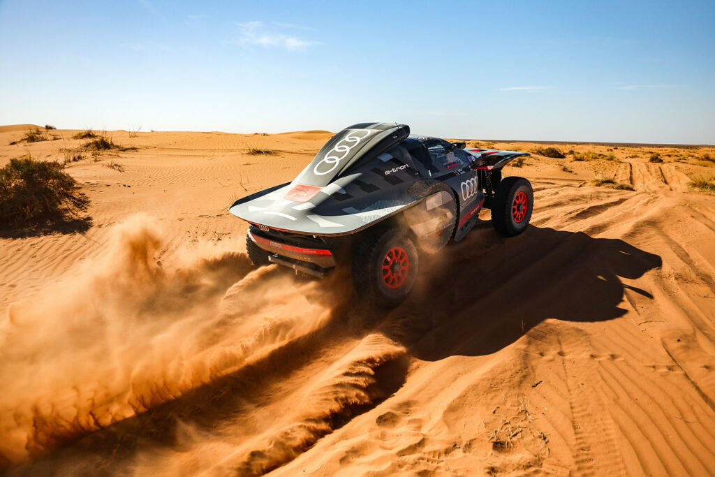 voiture audi rs q e-tron qui escalade une dune à pleine puissance dans le sable en vue du dakar 2024